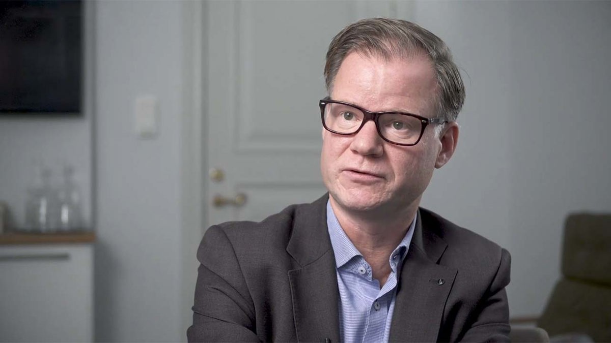 Person införd mörkgrå kavaj, blå skjorta och svartbågade glasögon.
