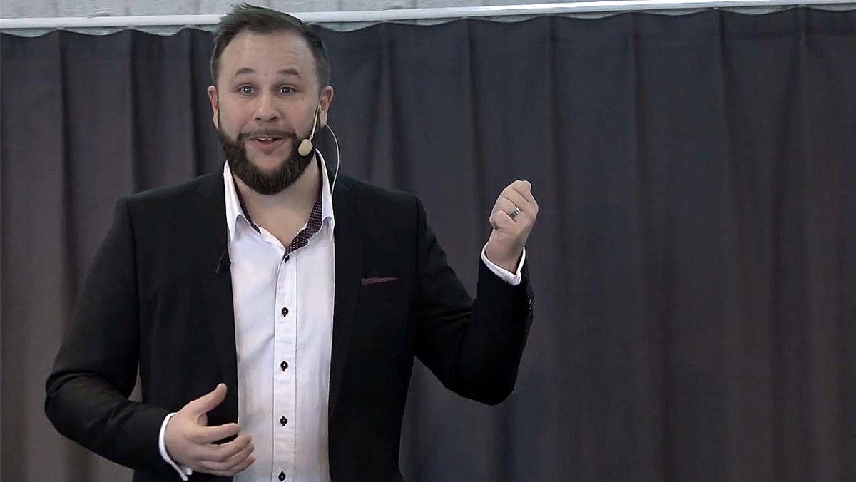 Person i seminariesituation iförd mikrofoneheadset stående framför ett mörkt draperi.
