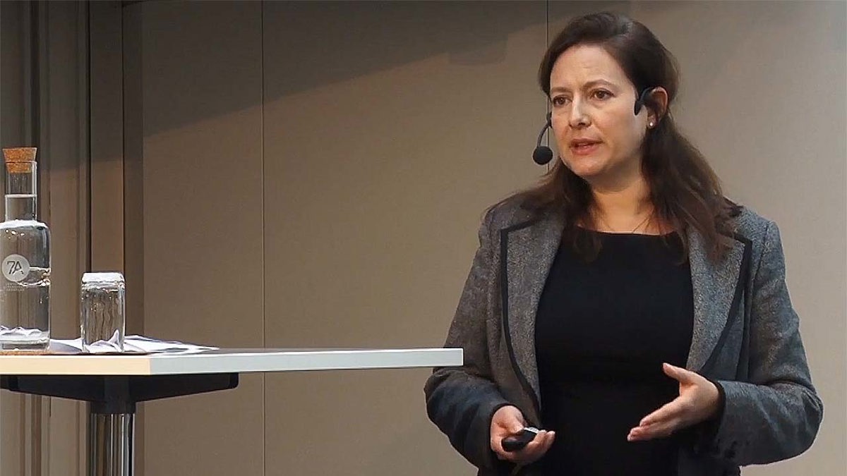 Person i seminariesituation stående bakom pulpet med vatten i en glasflaska och ett dricksglas.