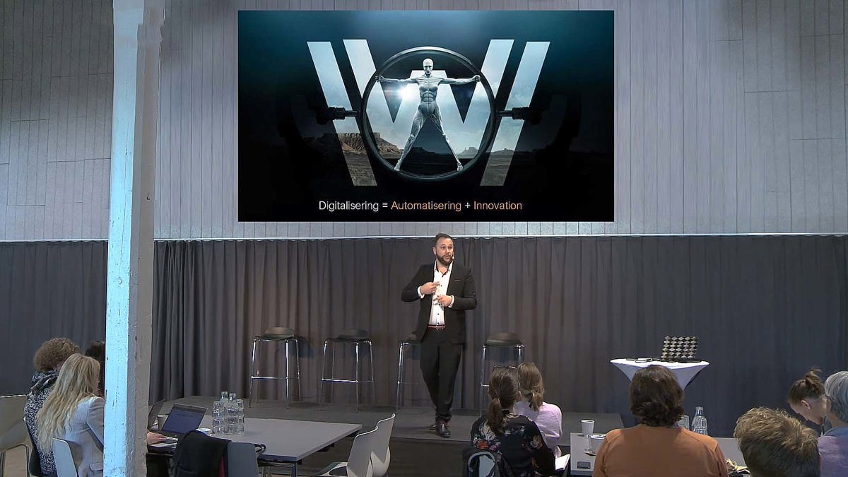 Person i seminariesituation iförd mikrofoneheadset stående framför ett mörkt draperi.